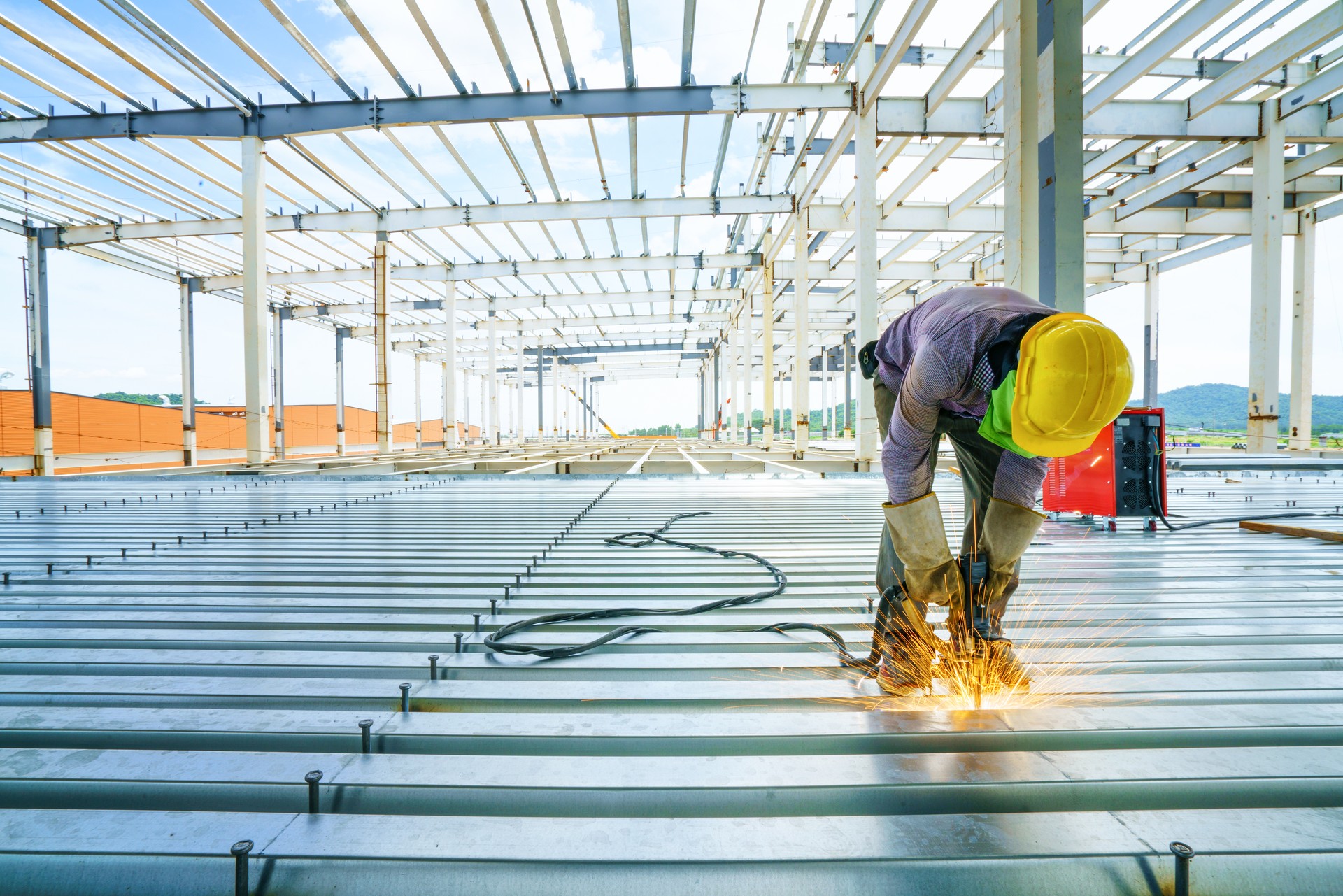 Welder are welds re-bar shear keys metal deck slab of mezzanine floor under the construction building in the factory with blue sky